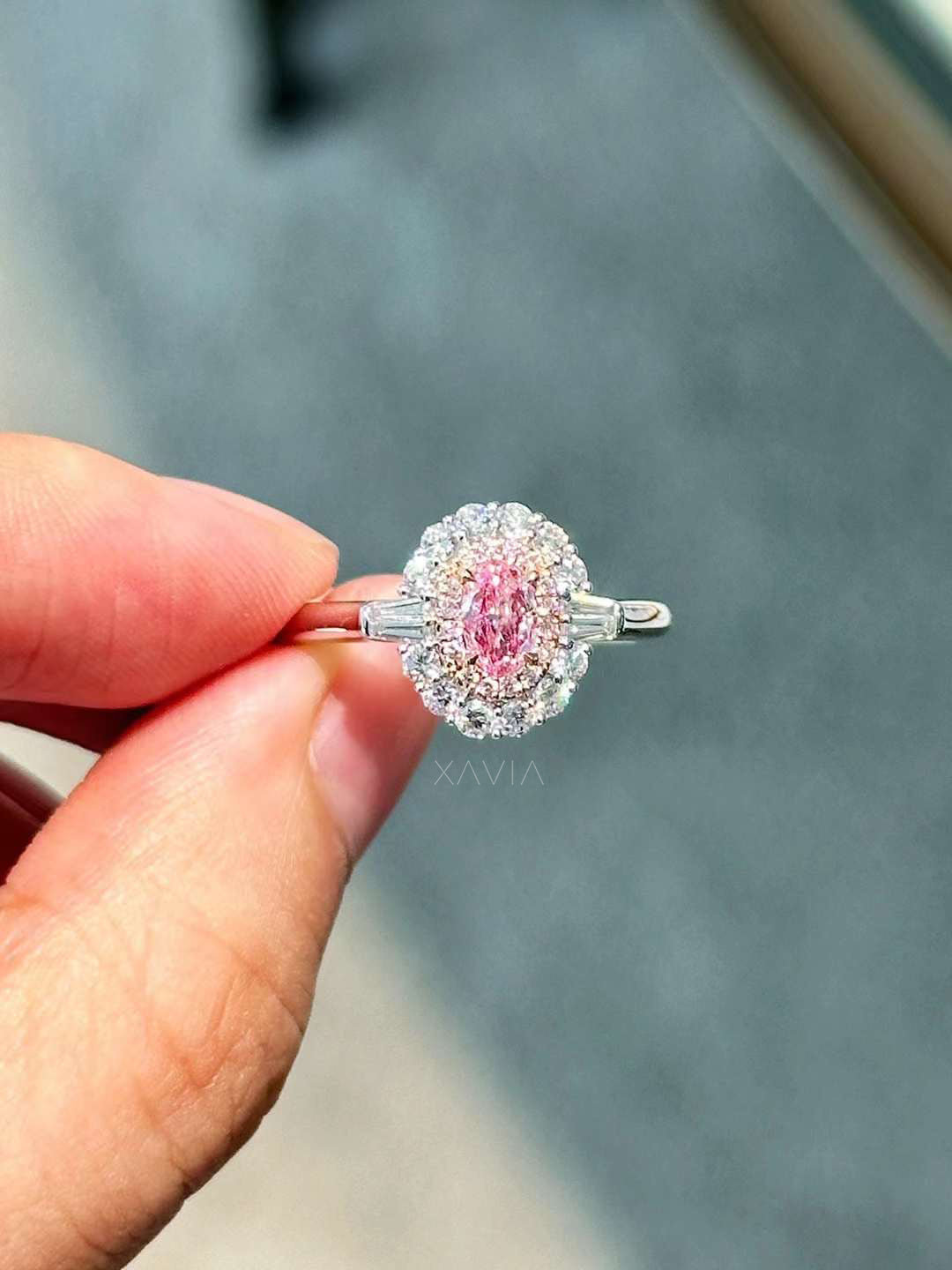 close-up view of pink oval lab diamond ring with white double halo and tapered baguette accents